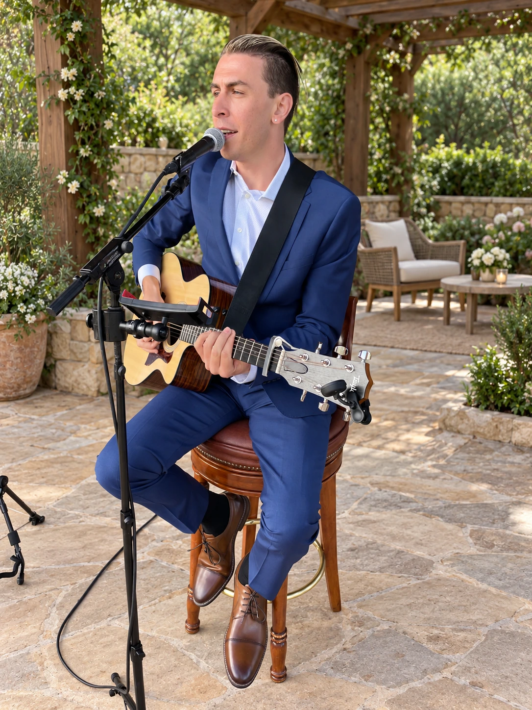 TREVAN singing and playing acoustic guitar in a navy suit, with an edited garden pergola background